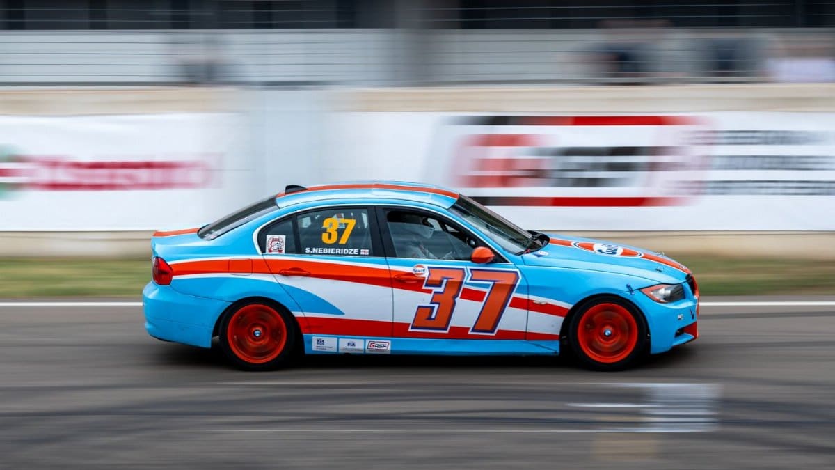 Blue and red race car speeding on the track during a daylight race event.
