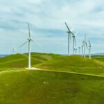 Wind turbines stand tall on lush green hills under a blue sky, generating clean energy in California's landscape.