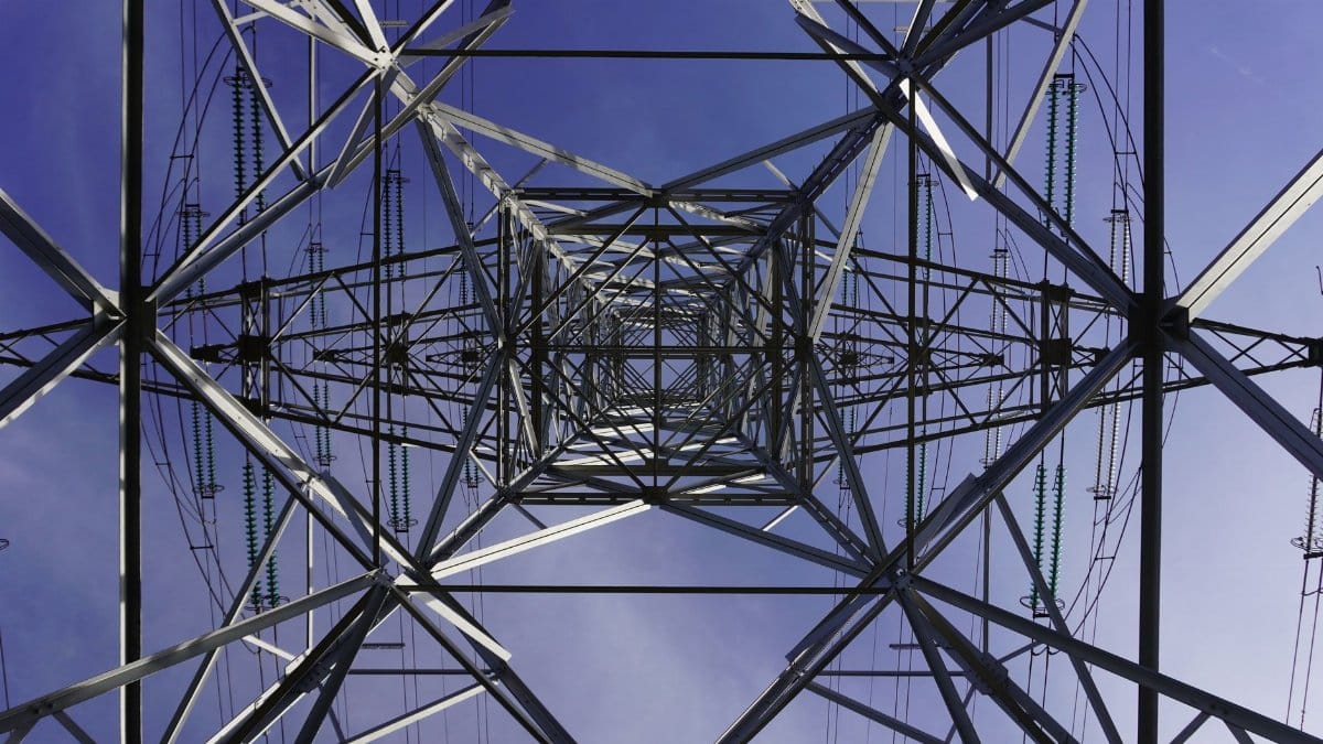 Low angle view of a transmission tower with geometric patterns against a clear blue sky.
