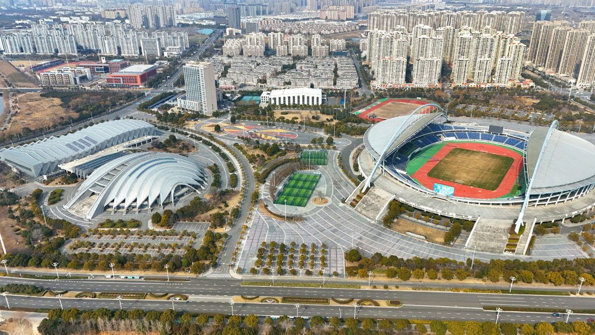 Aerial view showcasing a large stadium with modern architecture amidst an expansive urban setting.