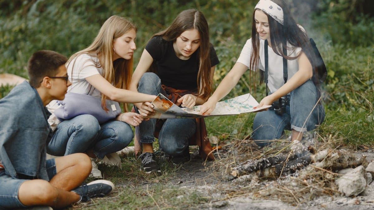 Group of teens sitting around a campfire, planning adventure with a map.