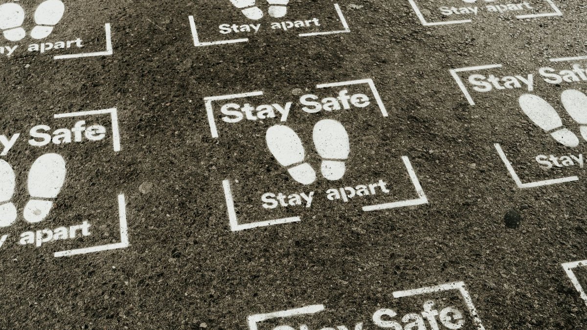 From above white sign of feet and inscription Stay Safe Stay Apart painted on asphalt road during coronavirus outbreak