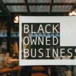 Black owned business sign taped on a window, seen from outside a store.