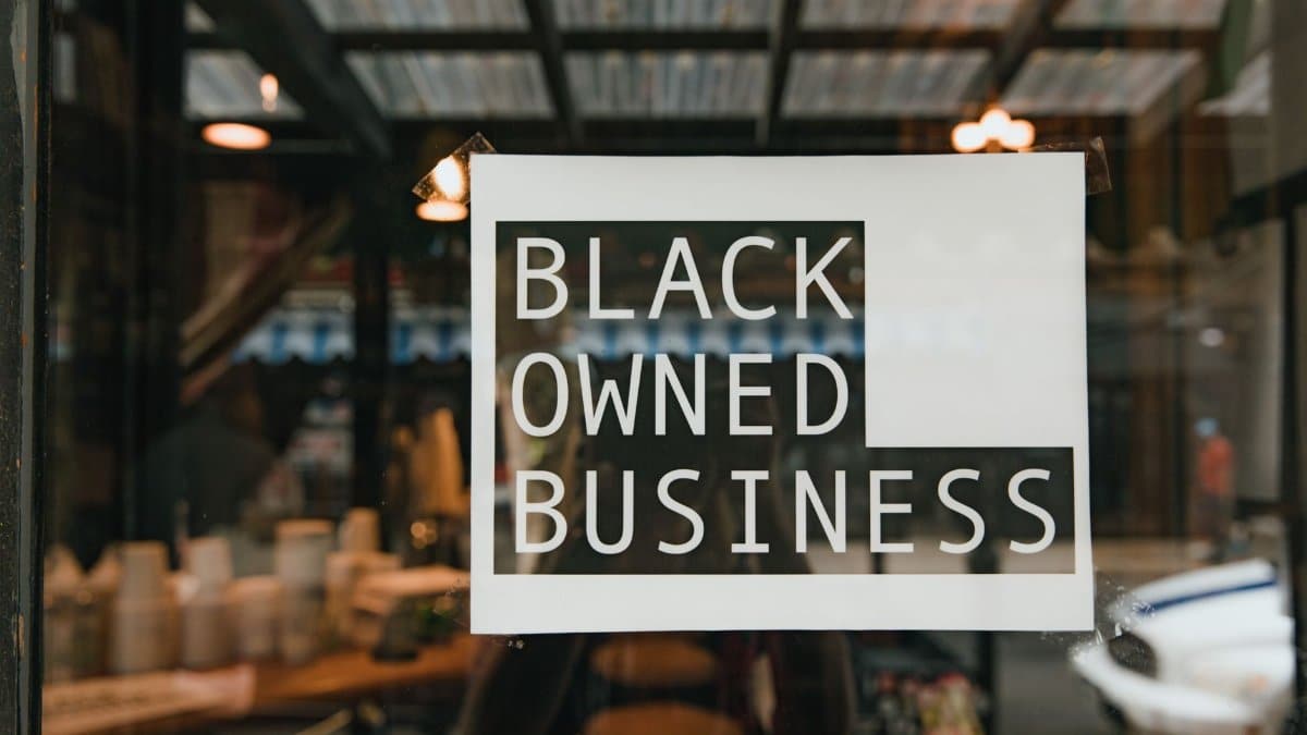 Black owned business sign taped on a window, seen from outside a store.