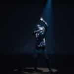 Dynamic image of a stylish performer dancing under a spotlight on stage, showcasing fashion and movement.