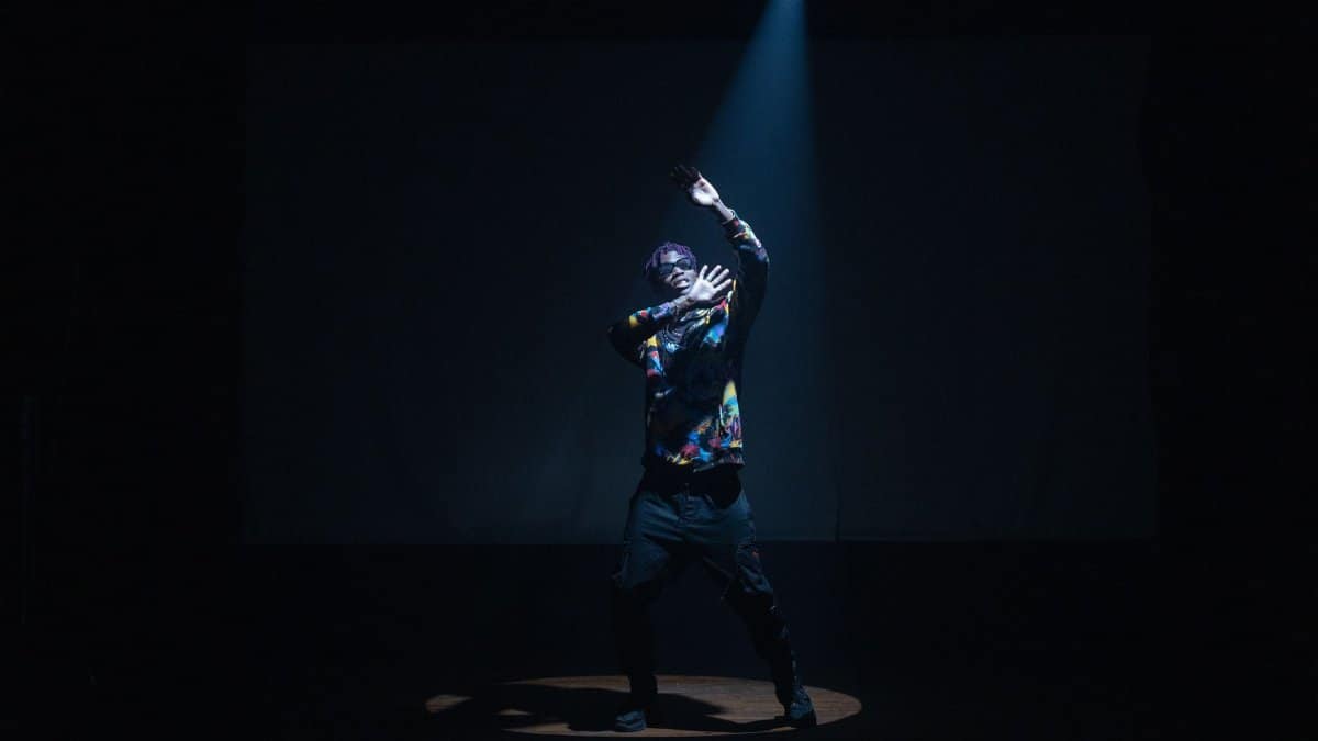 Dynamic image of a stylish performer dancing under a spotlight on stage, showcasing fashion and movement.
