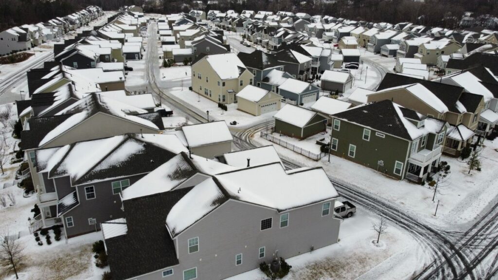 Drone view of suburban houses covered in snow during winter, showcasing a quiet residential neighborhood.