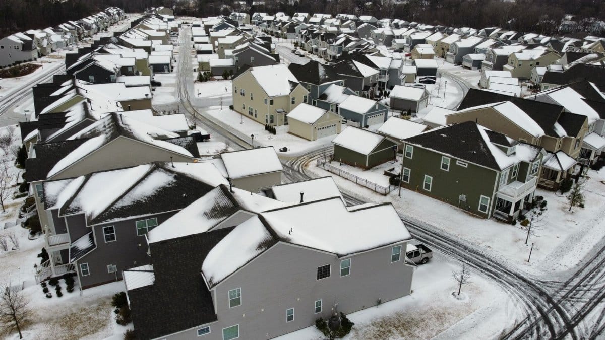 Drone view of suburban houses covered in snow during winter, showcasing a quiet residential neighborhood.