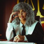 An elegant judge in robes sits at a desk in a courtroom, poised and authoritative.