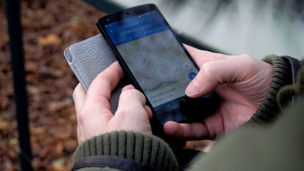 Close-up of hands using a map app on a smartphone outdoors, showcasing GPS navigation.