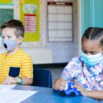 Two children wearing masks learn and play in a bright classroom setting, focusing on education and safety.