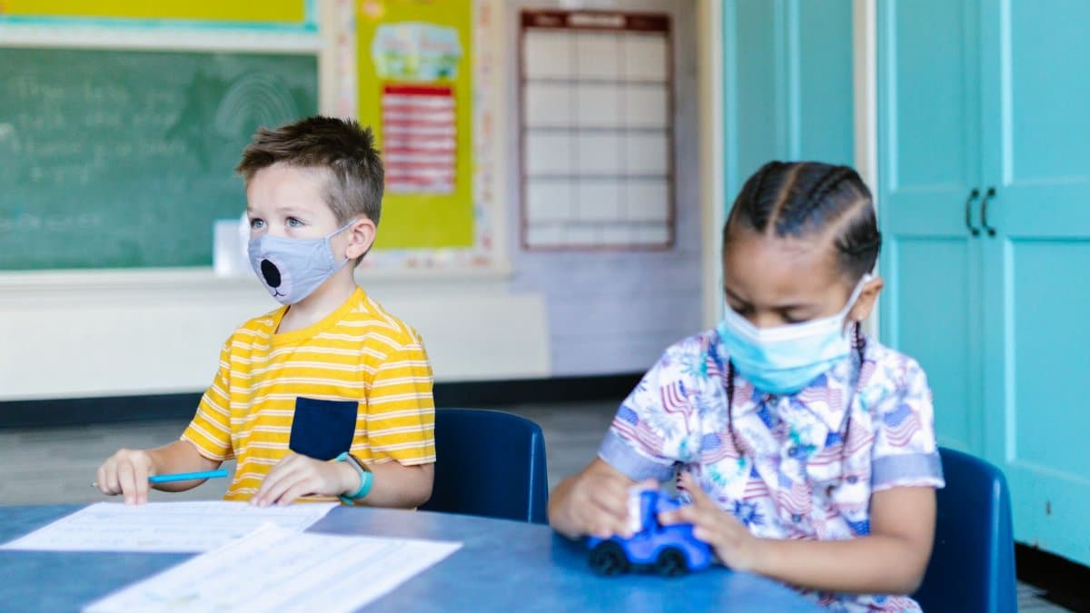 Two children wearing masks learn and play in a bright classroom setting, focusing on education and safety.