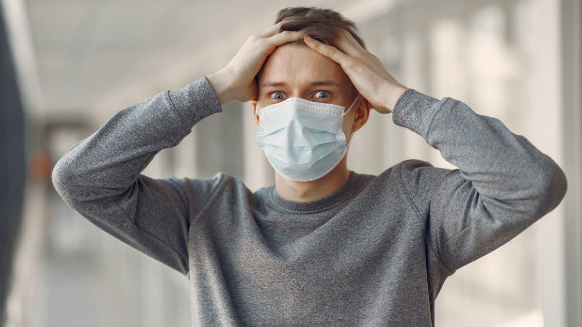 A man indoors wearing a face mask expressing shock and concern, highlighting the importance of health safety.