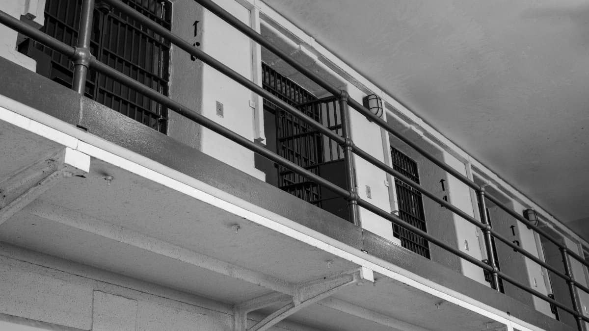 Monochrome view of prison cell block with barred doors and railing.