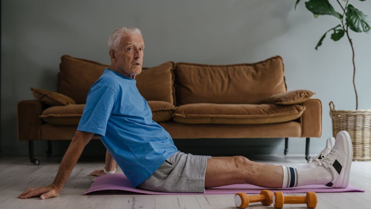 Senior man exercising indoors on a yoga mat with dumbbells. Health and fitness lifestyle.
