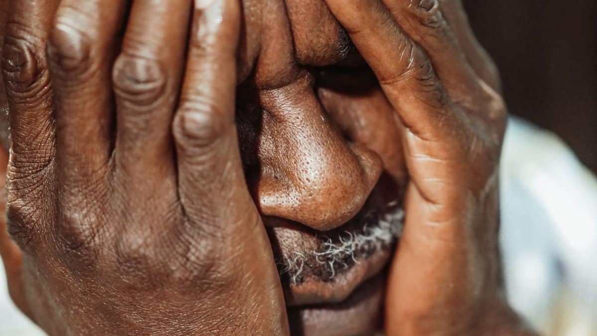 Close-up portrait of an elderly man with hands covering face, showing emotion.