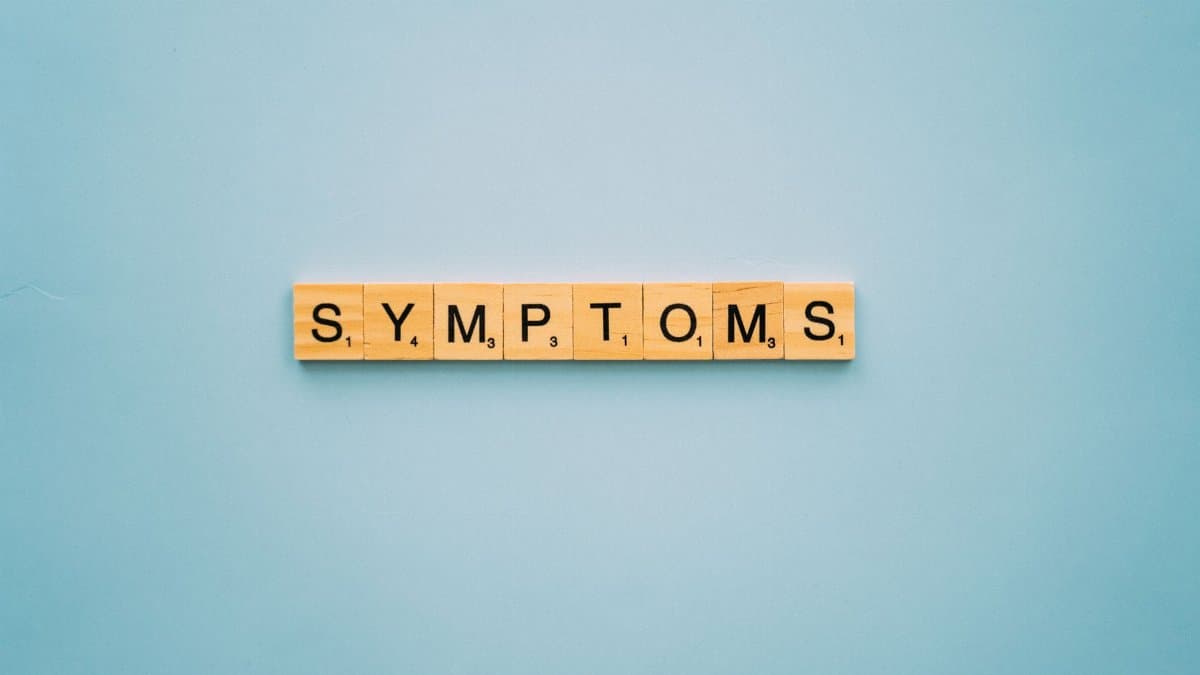 Scrabble tiles spelling 'SYMPTOMS' on a blue background, symbolizing health concepts.