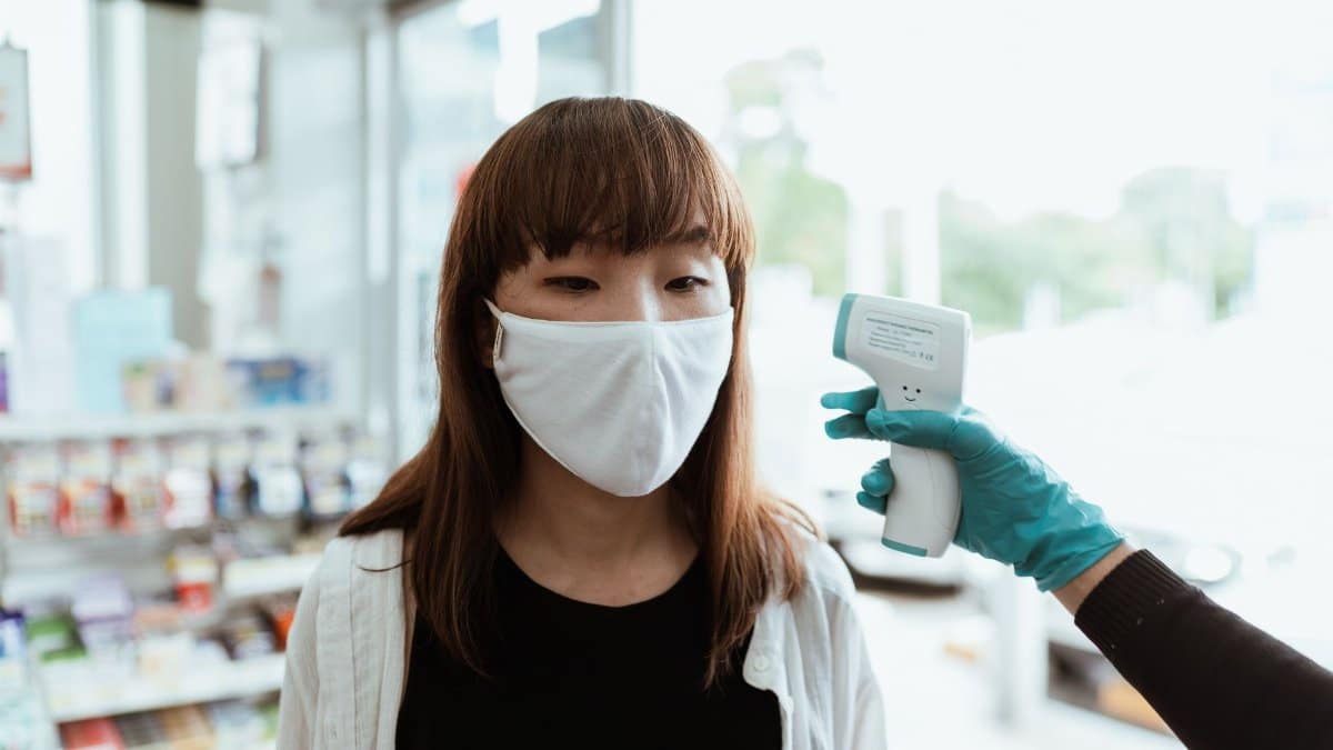 Woman in mask having temperature checked at store entrance amid pandemic precautions.
