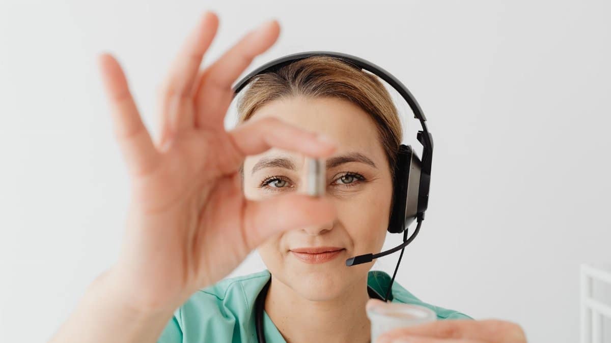 Female doctor in headset holding pill during online medical consultation, emphasizing telehealth.