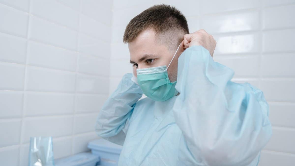 A male medical professional adjusting a face mask in a clinical setting.