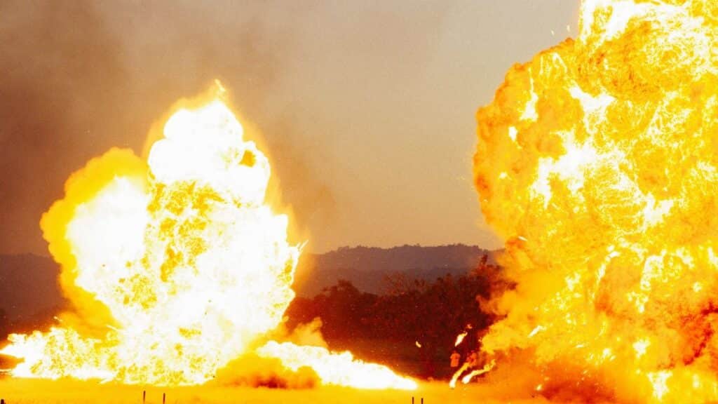 Powerful explosion with bright flames against an outdoor landscape, creating a dramatic visual impact.
