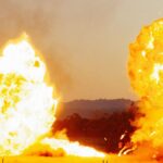 Powerful explosion with bright flames against an outdoor landscape, creating a dramatic visual impact.