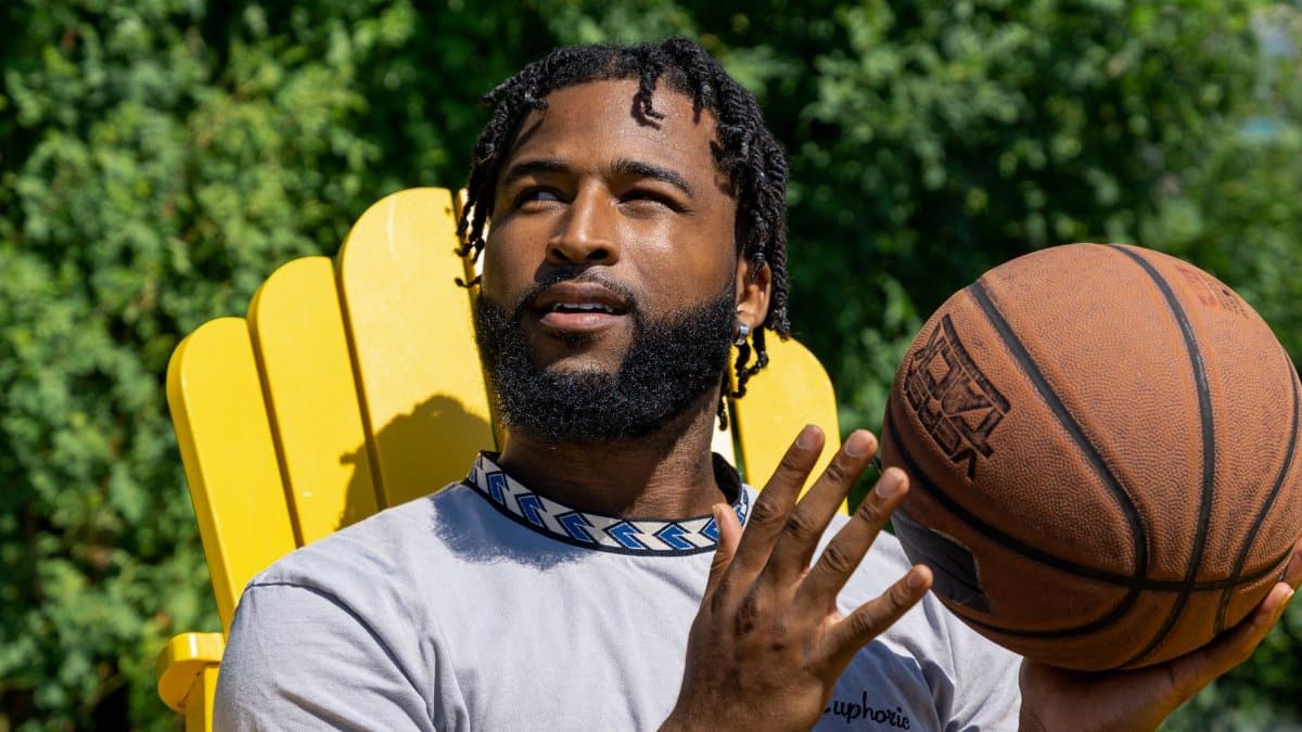 A young man sits outdoors holding a basketball, enjoying a sunny day.
