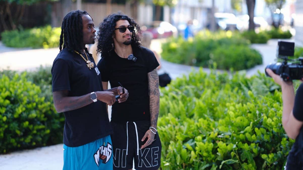 Two adults casually interacting outdoors during the day in a leafy urban setting.