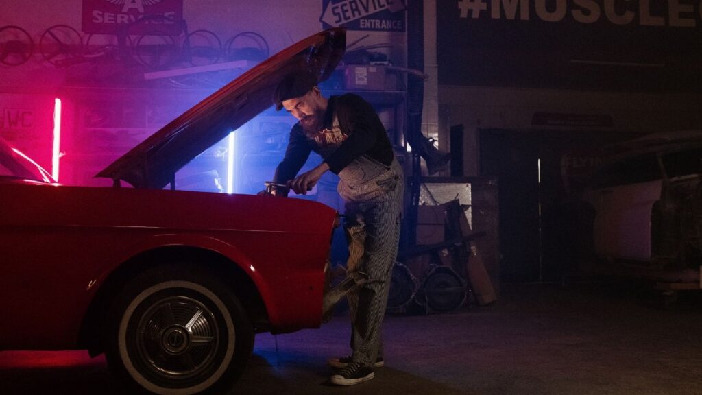 A mechanic working on a vintage car in a garage with colorful neon lights.