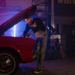 A mechanic working on a vintage car in a garage with colorful neon lights.
