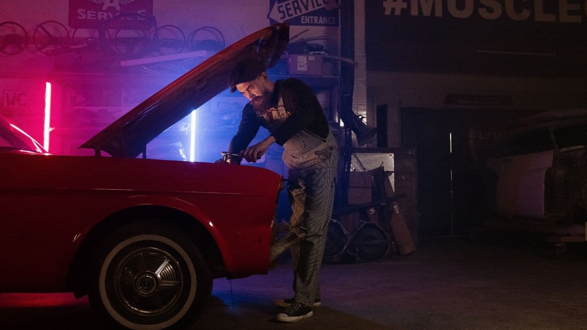 A mechanic working on a vintage car in a garage with colorful neon lights.