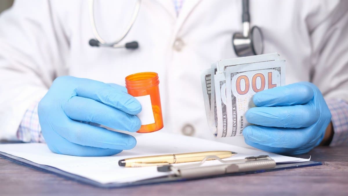 Doctor in gloves holding pill bottle and cash, highlighting medical expenses.