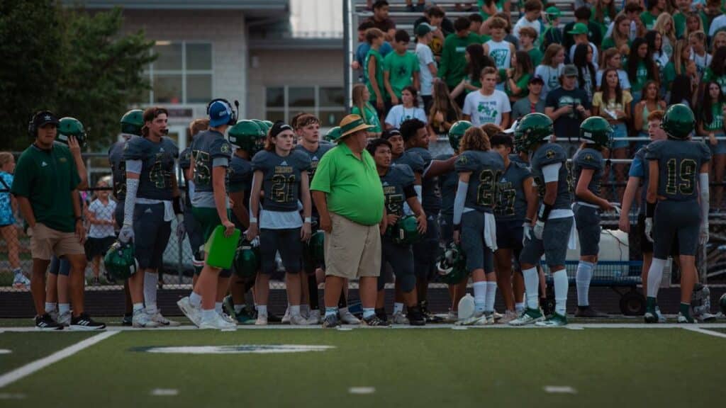 High school football players and coach on sidelines during a game.