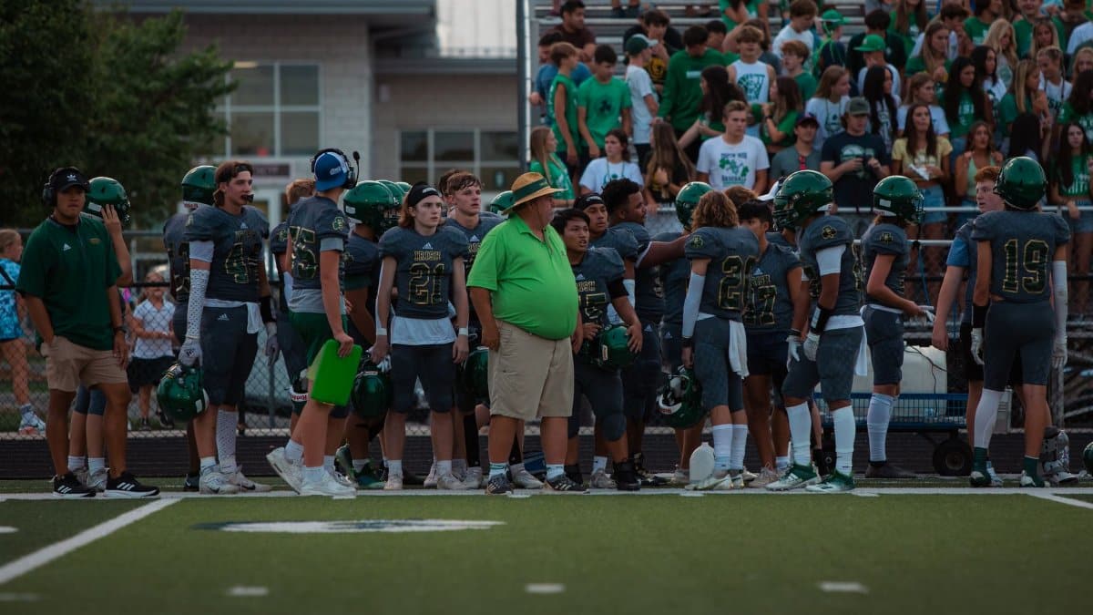 High school football players and coach on sidelines during a game.