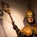 Illuminated statue of a bishop with a shadow cast on the wall in Holset, Limburg.