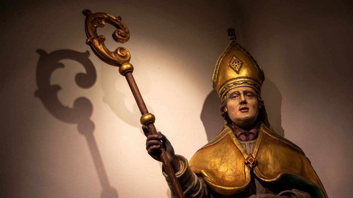 Illuminated statue of a bishop with a shadow cast on the wall in Holset, Limburg.