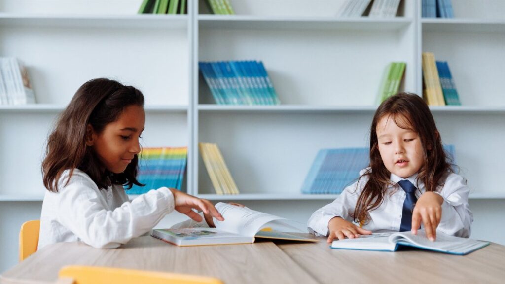 Two young girls enjoying books in a vibrant school library setting.