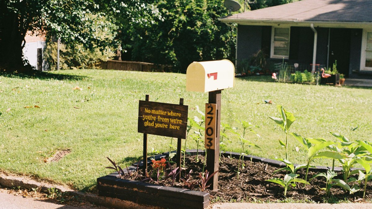 Suburban house with plants and welcoming sign by mailbox on a sunny day.