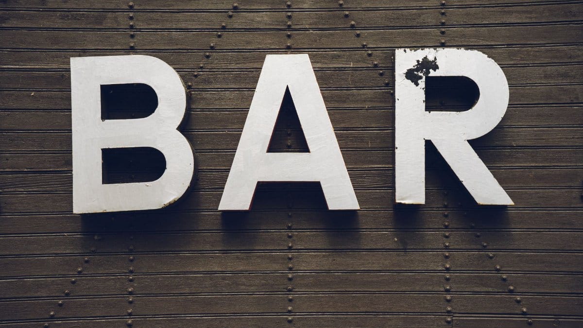 A rustic vintage bar sign painted on a wooden textured wall.
