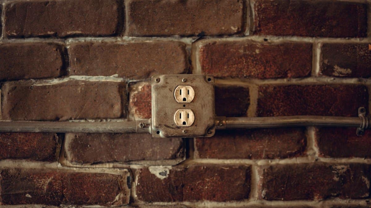Rustic exposed brick wall featuring aged electrical sockets and metal conduit.