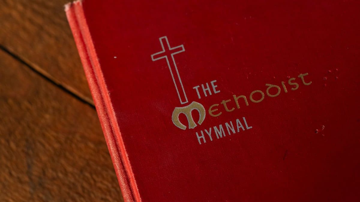 A red Methodist hymnal book with a cross symbol on a wooden table.