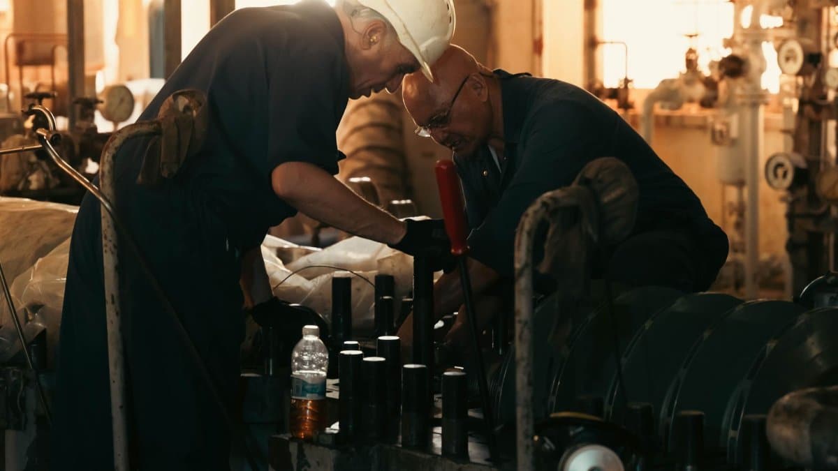 Two engineers collaborating on machinery maintenance in a dimly lit industrial plant.
