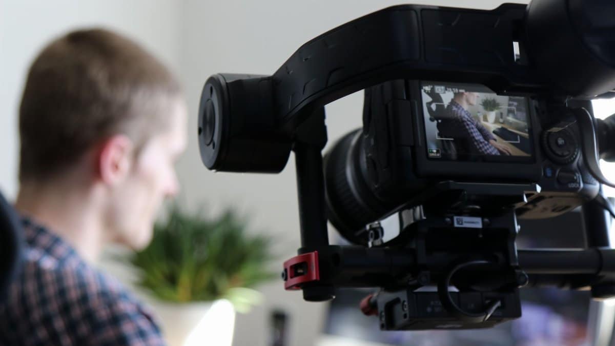 Close-up of camera filming a man in an indoor setting, highlighting professional video production