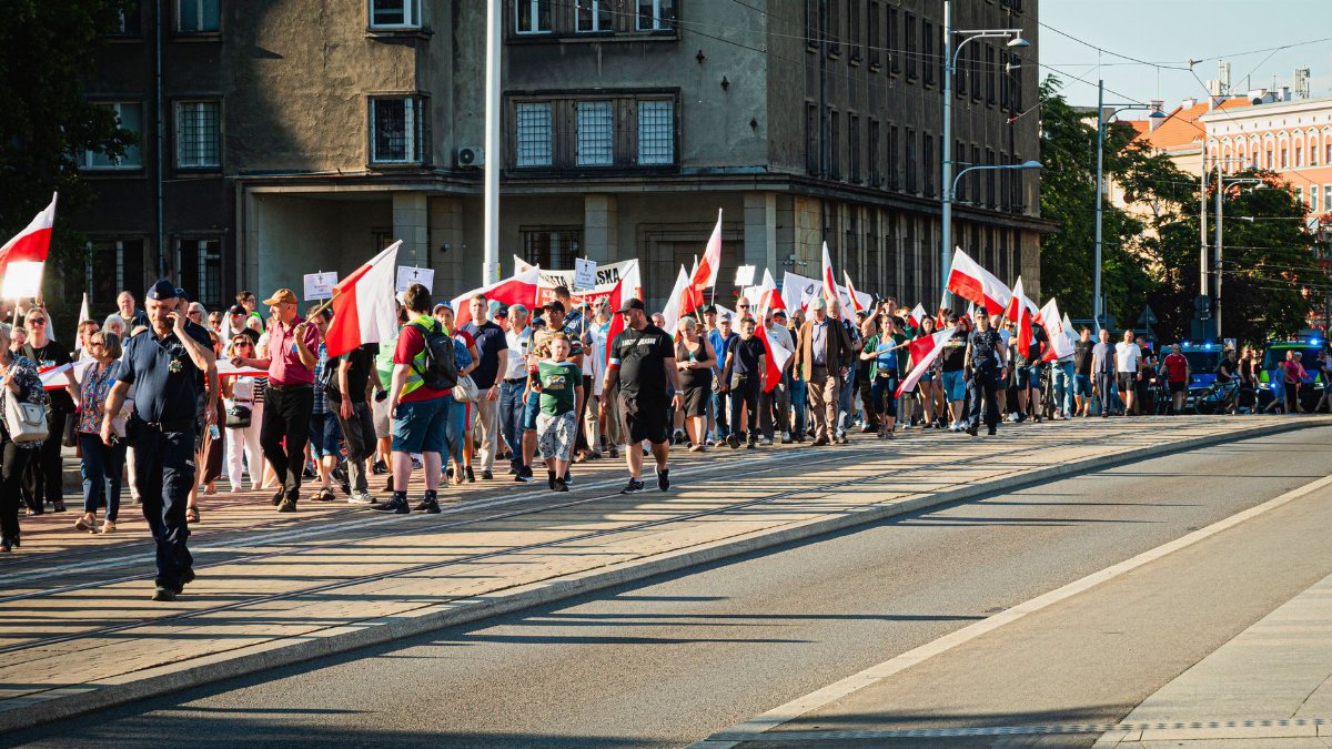 People marching in Wrocław with Polish flags honoring historical events. Captured in daylight.