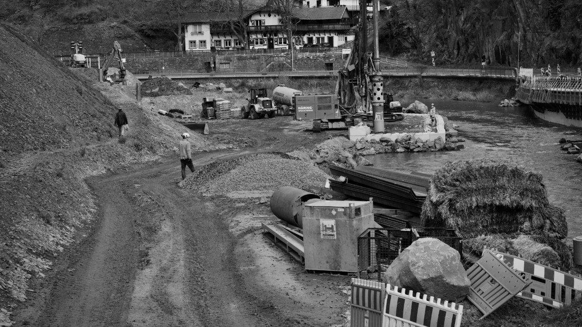 Monochrome image of construction site next to a river with heavy machinery and workers.