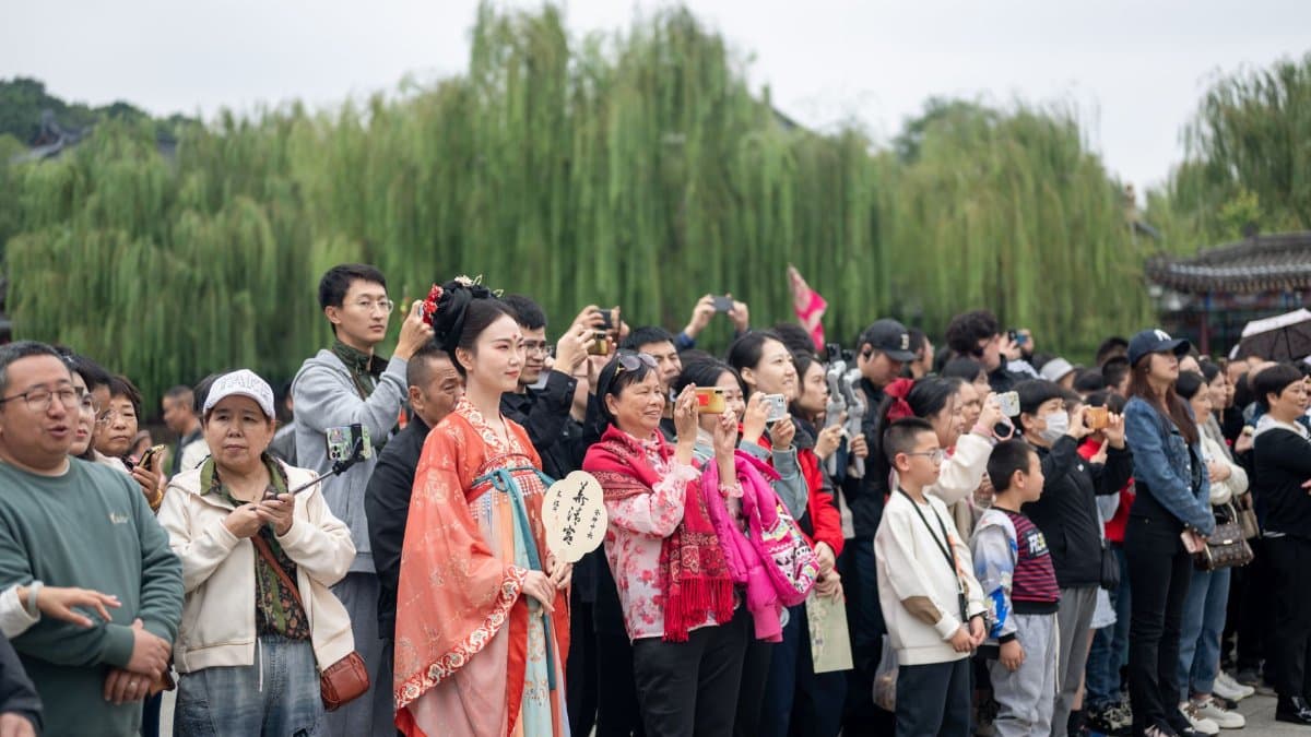 People gathered outdoors, one in traditional Chinese attire, observing an event.