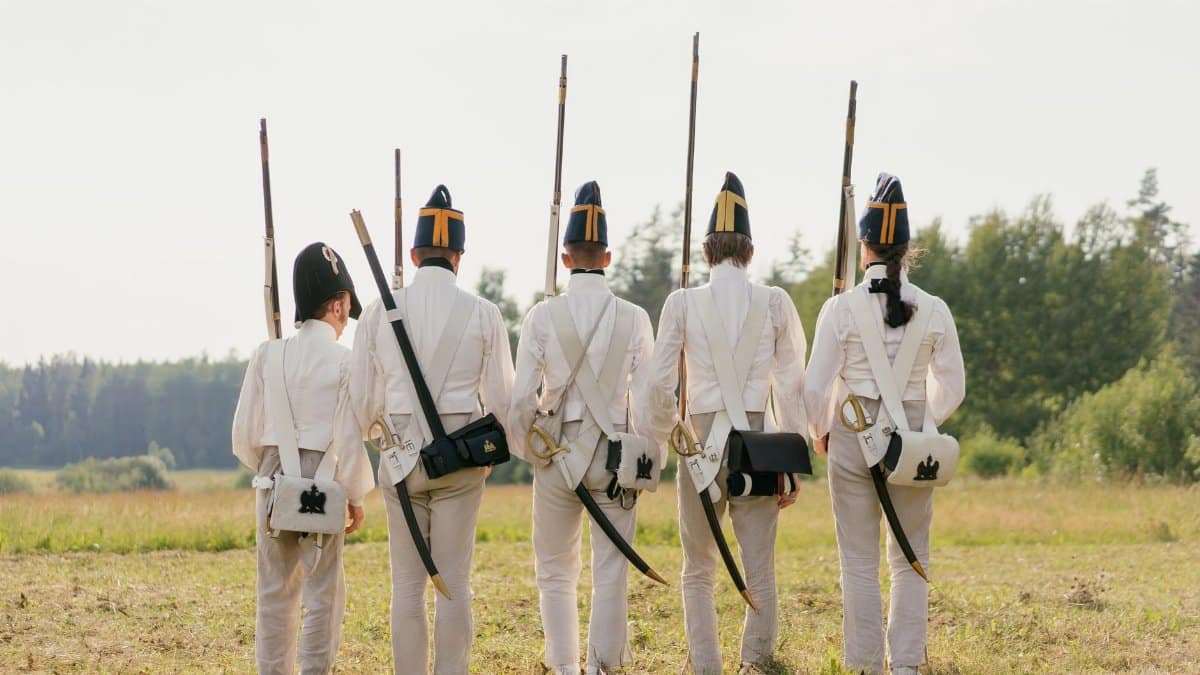 Back view of soldiers in historical uniforms with rifles during a reenactment.