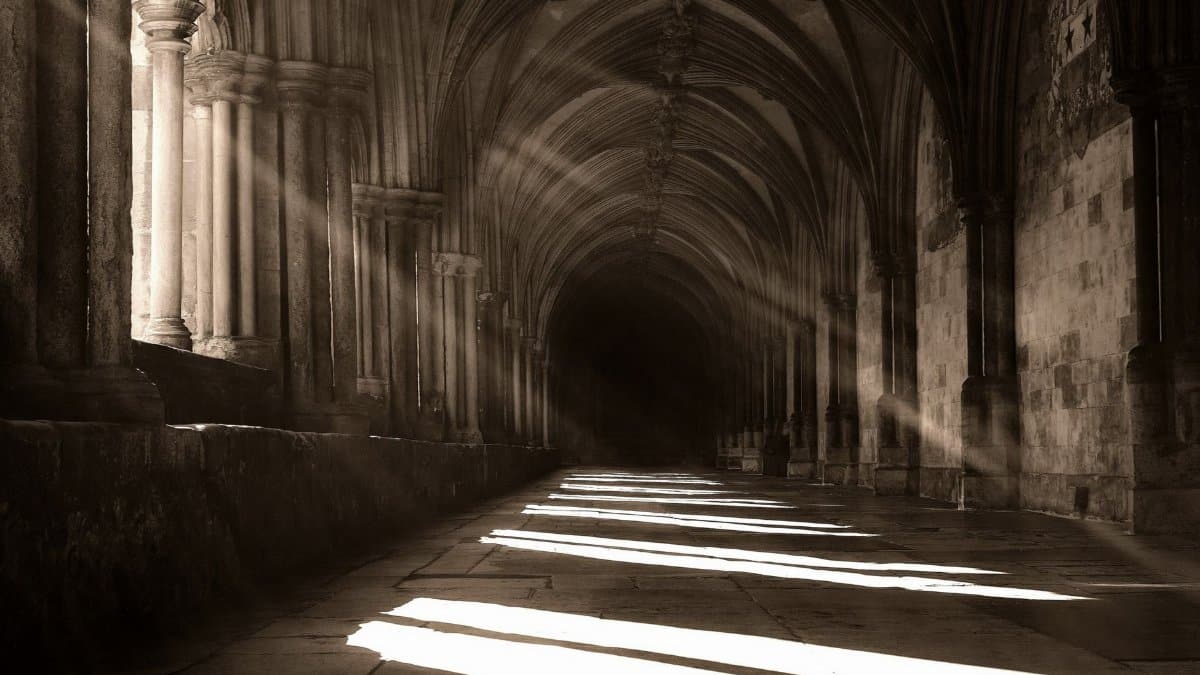 Sunbeams create intriguing shadows in a historical stone hallway, captured in black and white.