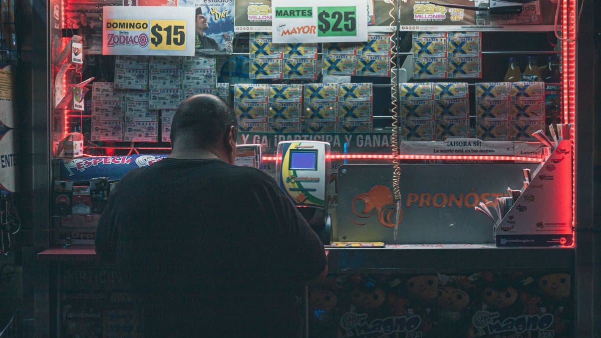 A man purchasing a lottery ticket at an illuminated kiosk in Mexico City, highlighting risk and hope.