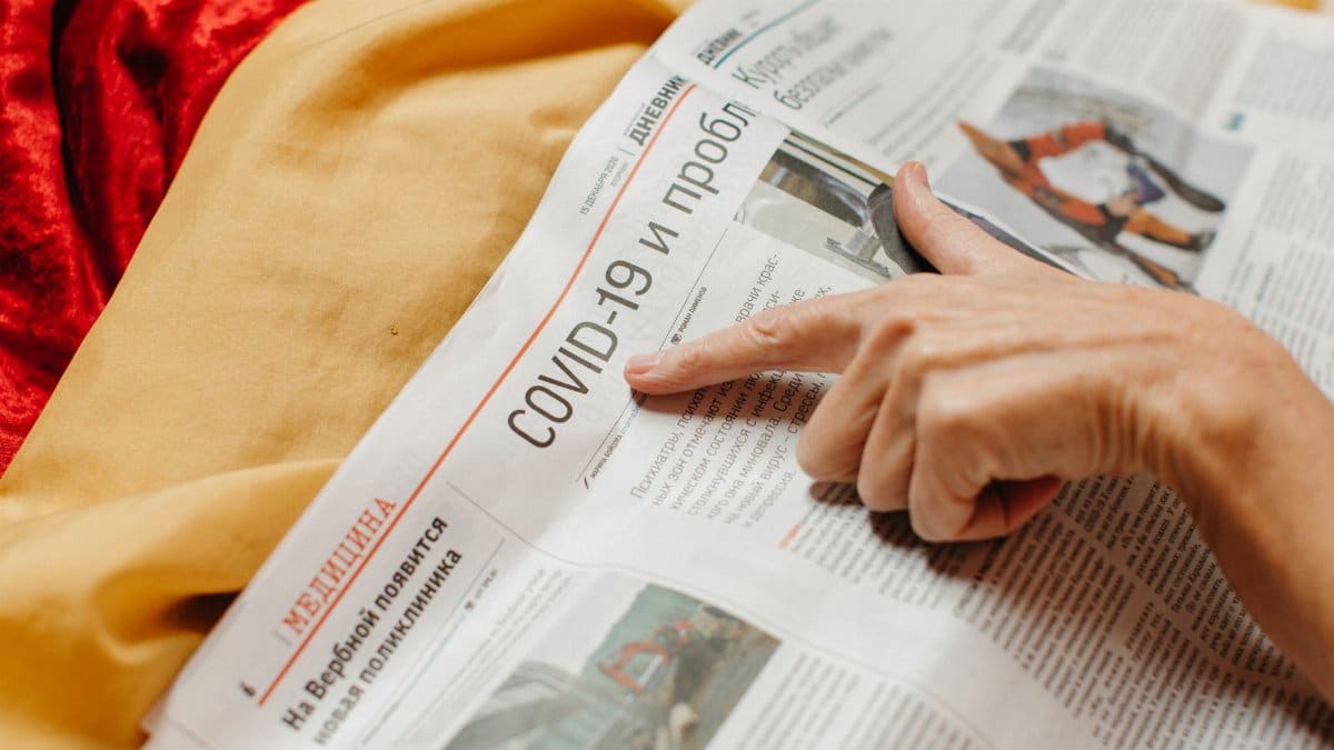 A close-up shot of a hand pointing at a COVID-19 headline in a newspaper.